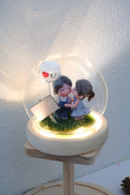 Decorative scene with a couple and a ballon inside a glass dome on a wooden stand.