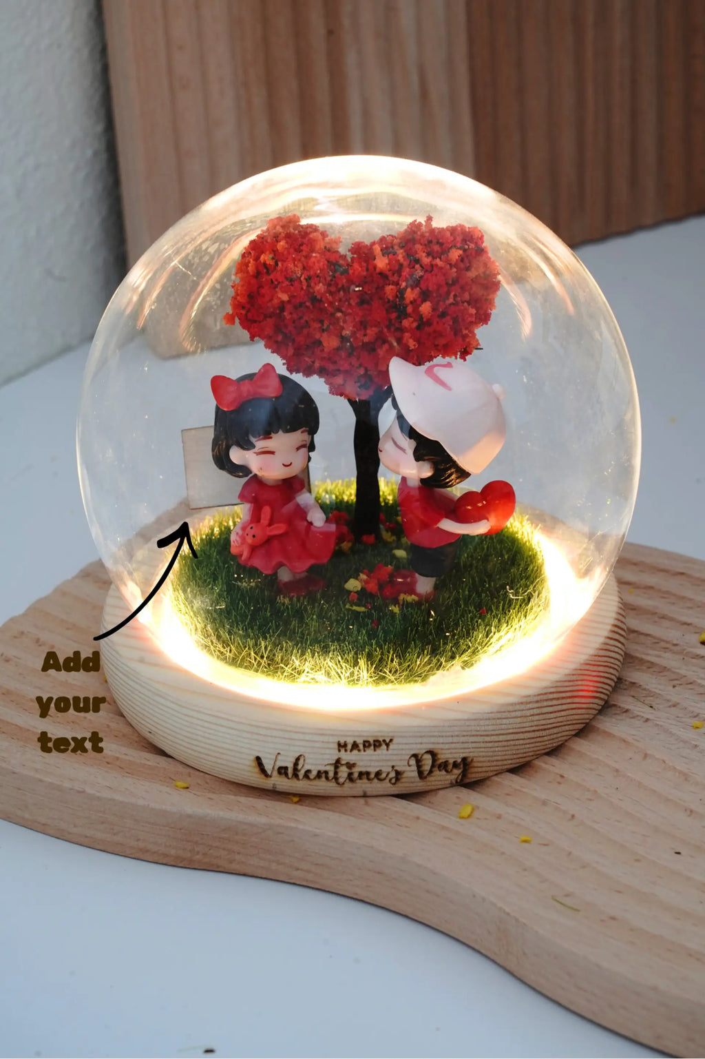 Valentine's crystal ball in round glass dome with LED lighting, displaying couple miniatures and two customisable engraving locations on wooden signboard and base