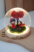 Valentine's crystal ball in round glass dome with LED lighting, displaying couple miniatures and two customisable engraving locations on wooden signboard and base