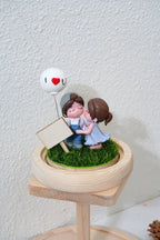 Decorative figurine of a couple with a heart balloon on a small stand.